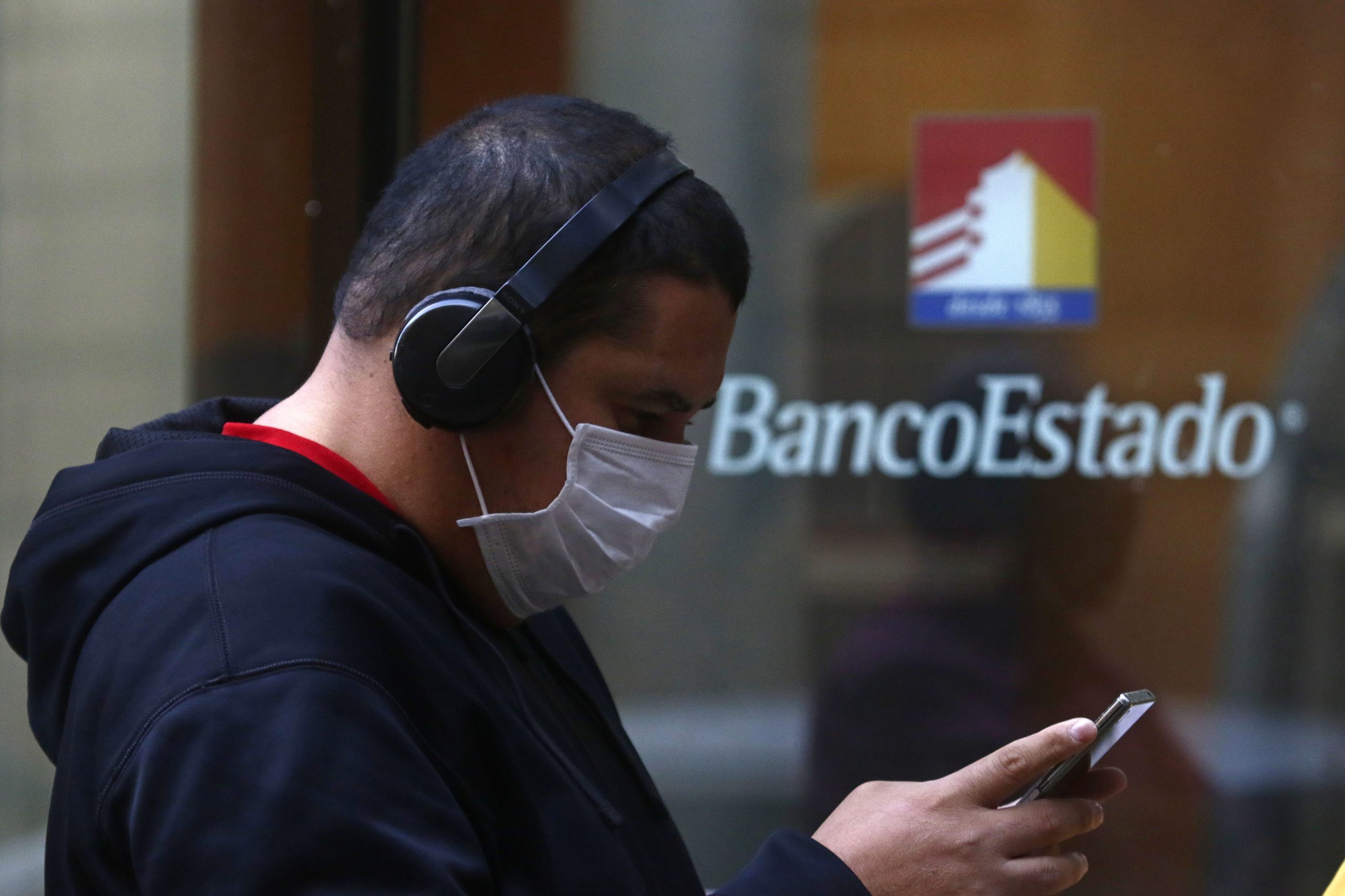 Joven revisando el celular con logo de BancoEstado de fondo.