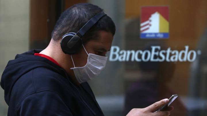 Hombre con audífonos mirando su celular a las afueras de una sucursal de BancoEstado de Chile