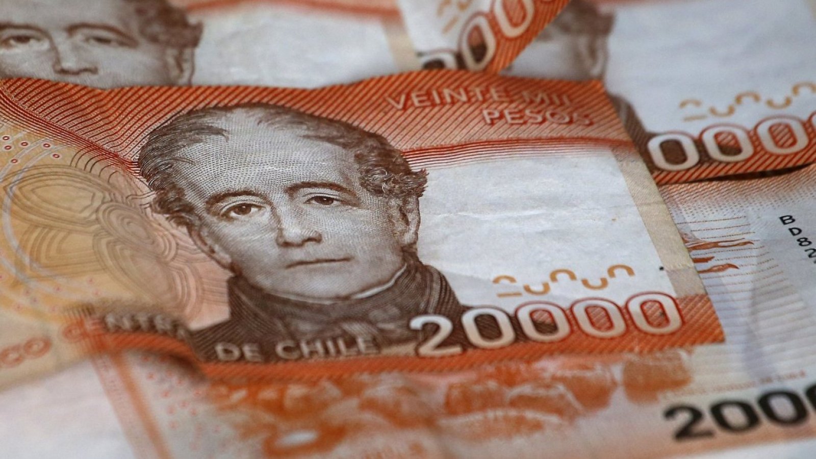 Billetes naranjos de 20 mil pesos apilados uno sobre otro.