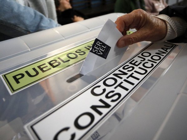 Mano ingresando voto en una urna electoral, en donde se lee 