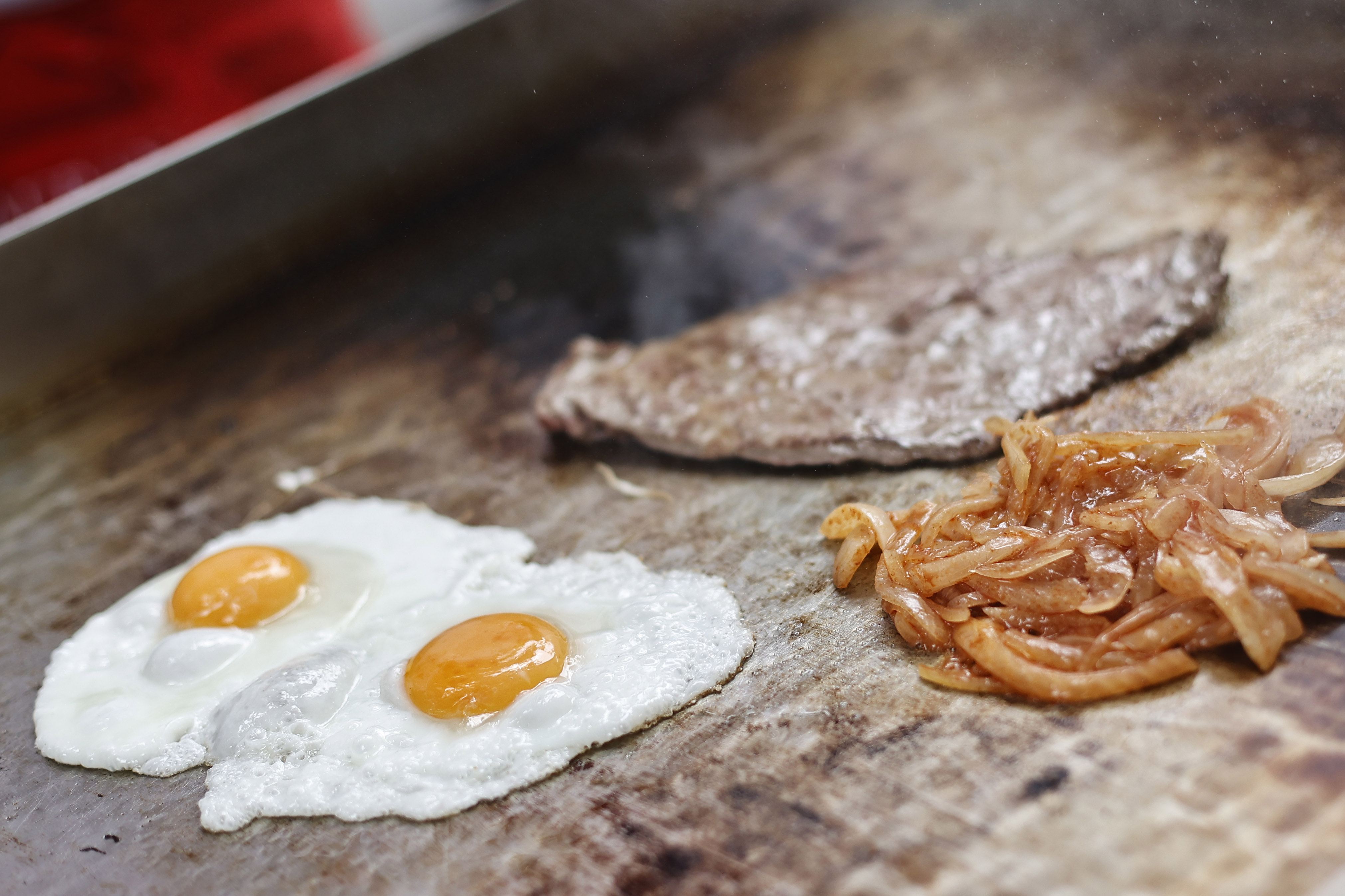 Huevos, carne y cebolla en una plancha, para preparar bistec a lo pobre.