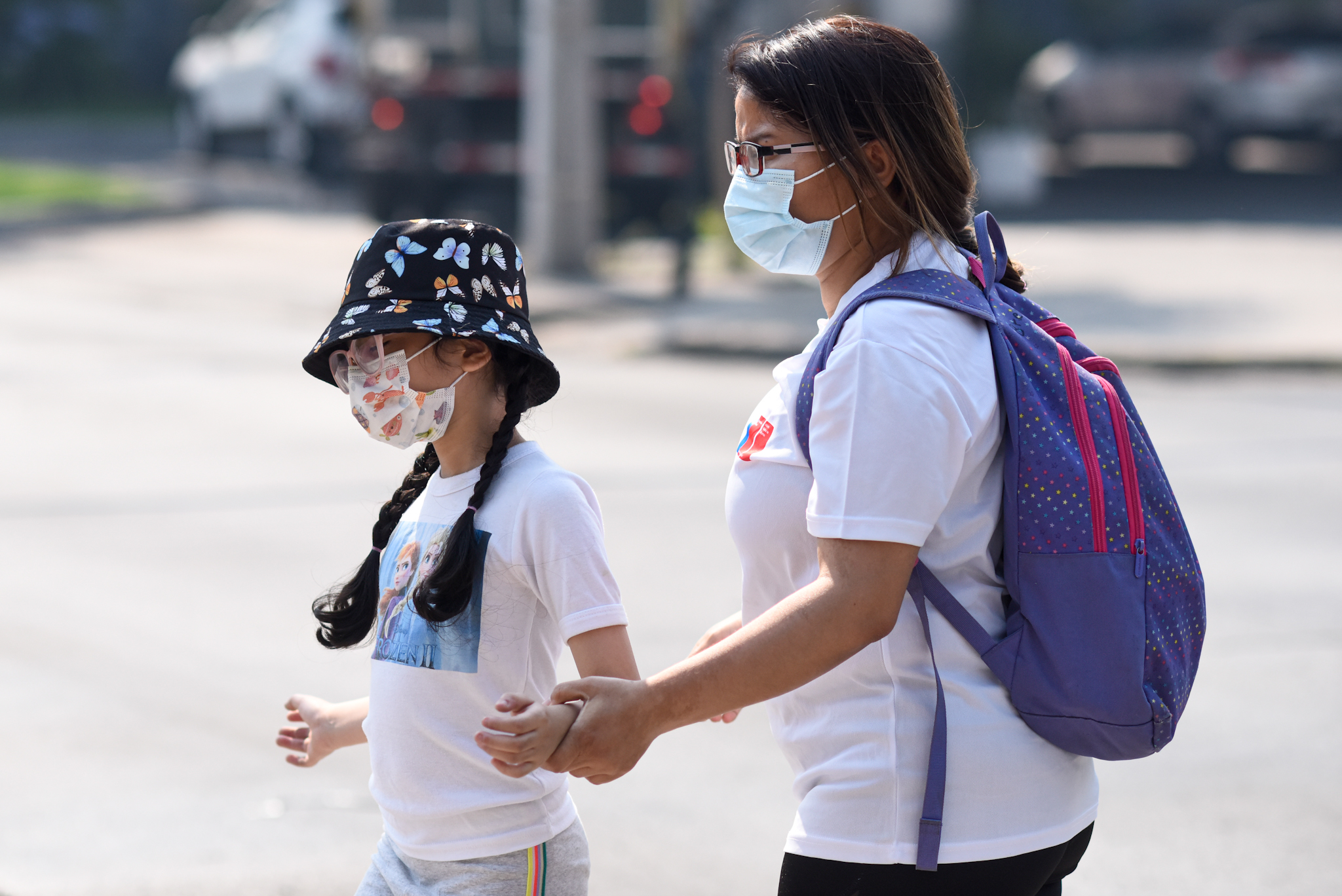 Niña y mamá con mascarilla caminando en la calle.