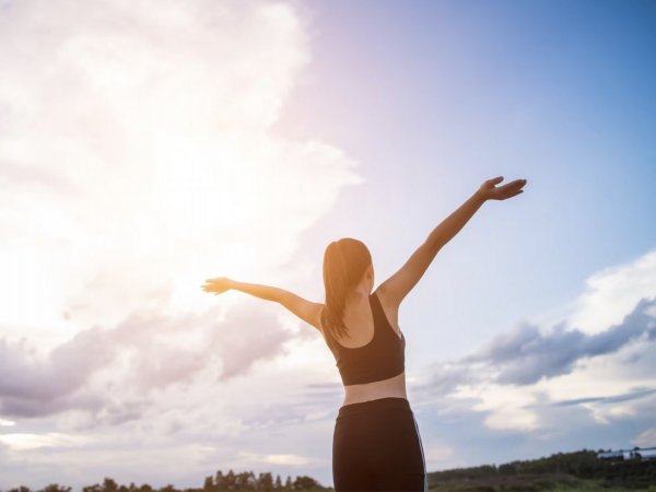 Mujer de espaldas con los brazos abiertos mirando al horizonte.
