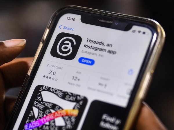 Mano sujetando un teléfono descargando la app de Threads.