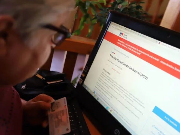 Persona mayor leyendo información de la PGU en un computador.