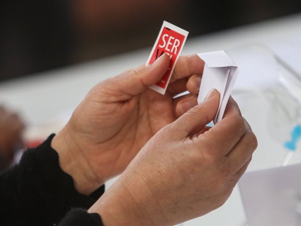 Mano sujetando voto electoral con sticker del SERVEL.