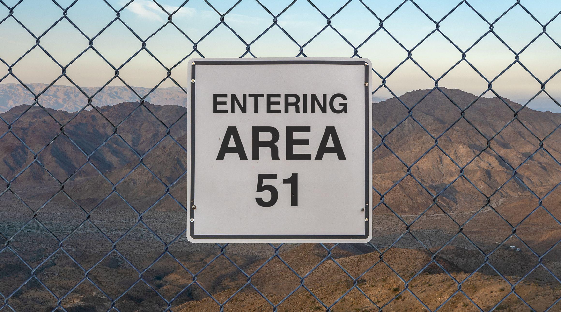 Cartel que dice "entrada al área 51" colocado en una verja entre las montañas de nevada 