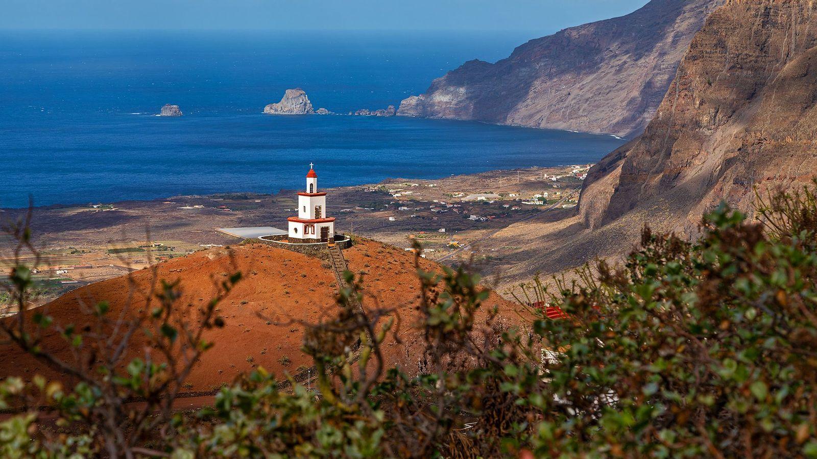 Faro rojo en medio de una isla verde y volcánica.