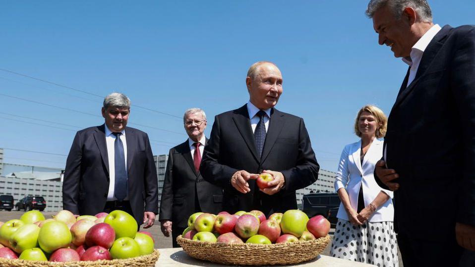 Putin delante de un cesto de manzanas.