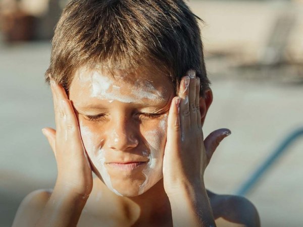Una playa con turistas aplicando protector solar, con el mar de fondo, resaltando el impacto de los químicos en el agua.