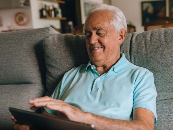Persona mayor usando un smartphone en casa, concentrada y sonriente, como símbolo del vínculo positivo entre tecnología y salud cognitiva.