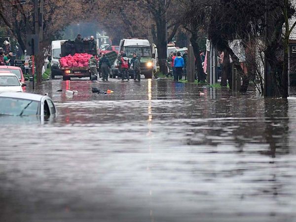 Vista aérea de Santiago tras una inundación, acompañada del titular del estudio que relaciona eventos climáticos extremos con crisis sociales en Chile.