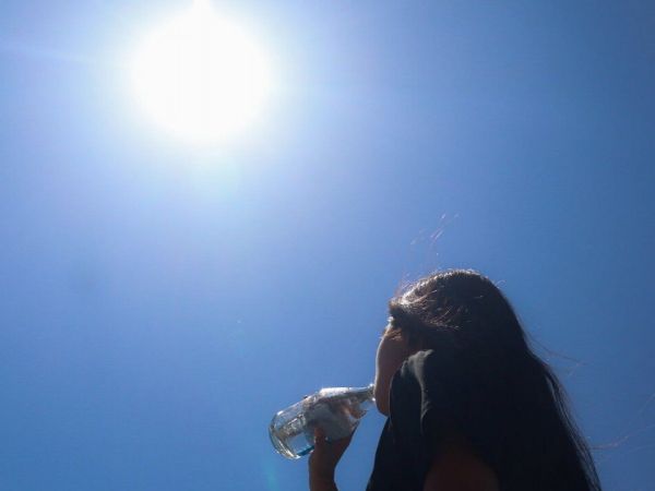 Mujer de espaldas a la cámara bebiendo una botella de agua bajo el sol