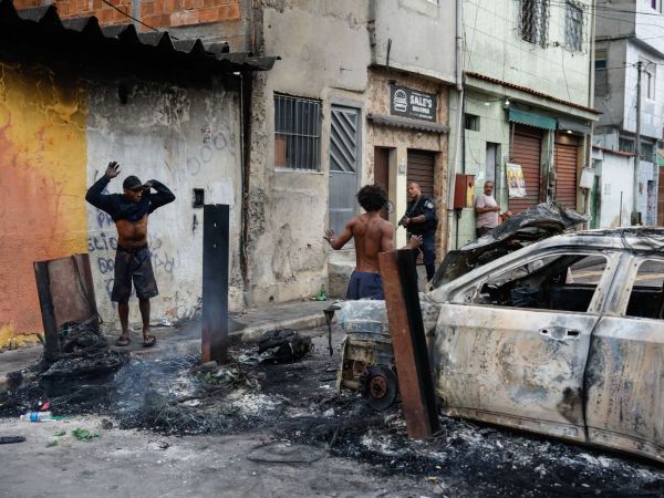 Policía con arma en la calle, auto quemado y hombres con los brazos arriba en medio de operativo.