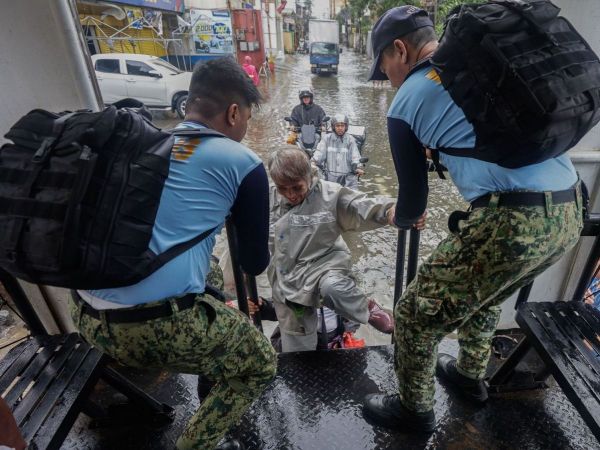 Dos personas con uniformes oficiales ayudan a damnificados en el paso del tifón en Filipinas.