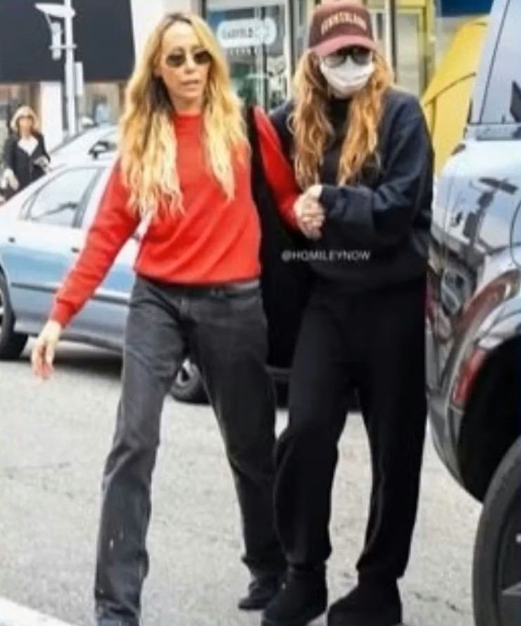 Miley Cyrus usando mascarilla y recibiendo ayuda de su madre para caminar