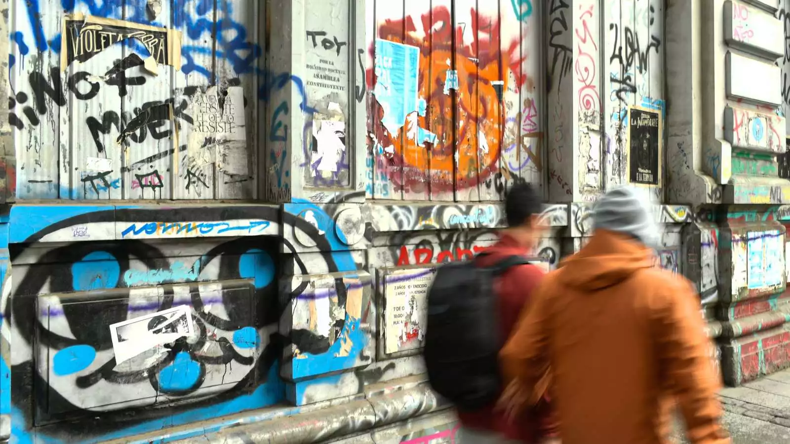 Muro rayado mientras transeúntes transitan por las calles de Valparaíso.