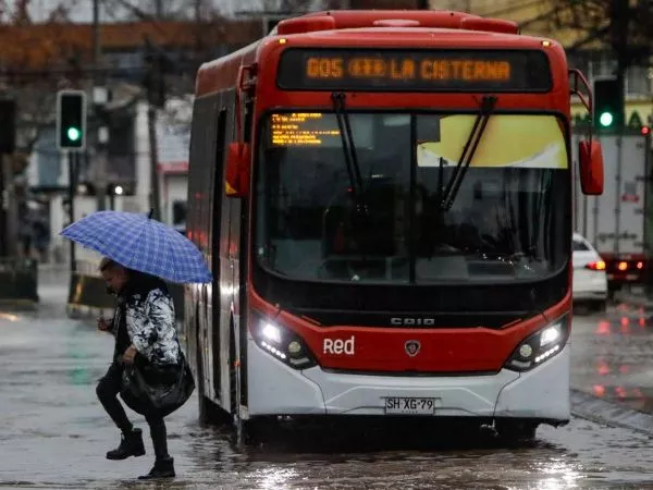 Persona cruzando la calle con paraguas frente a un bus del sistema RED de la Región Metropolitana.